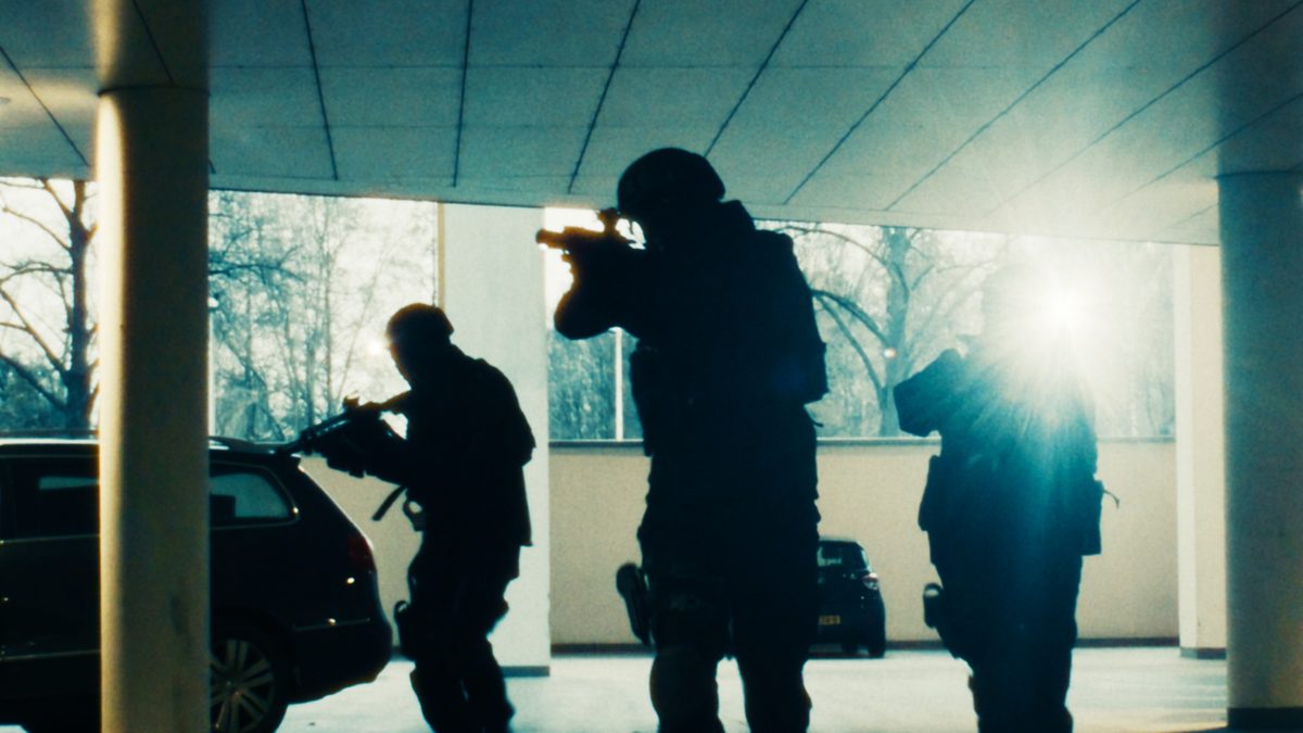 Een arrestatieteam in silhouet rukt met getrokken wapens op door een parkeergarage, in tegenlicht. Still uit een MediaTuig-commercial, 2024.