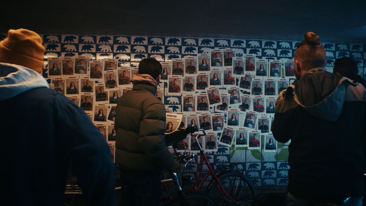 Mensen, op de rug gezien, voor een muur vol WANTED-posters. Still uit een MediaTuig-commercial, 2024.